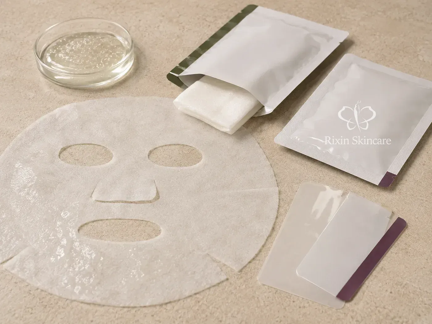 Unfolded and folded facial mask sheets arranged with clear essence, sealed sachets, and pouch-film samples for system review